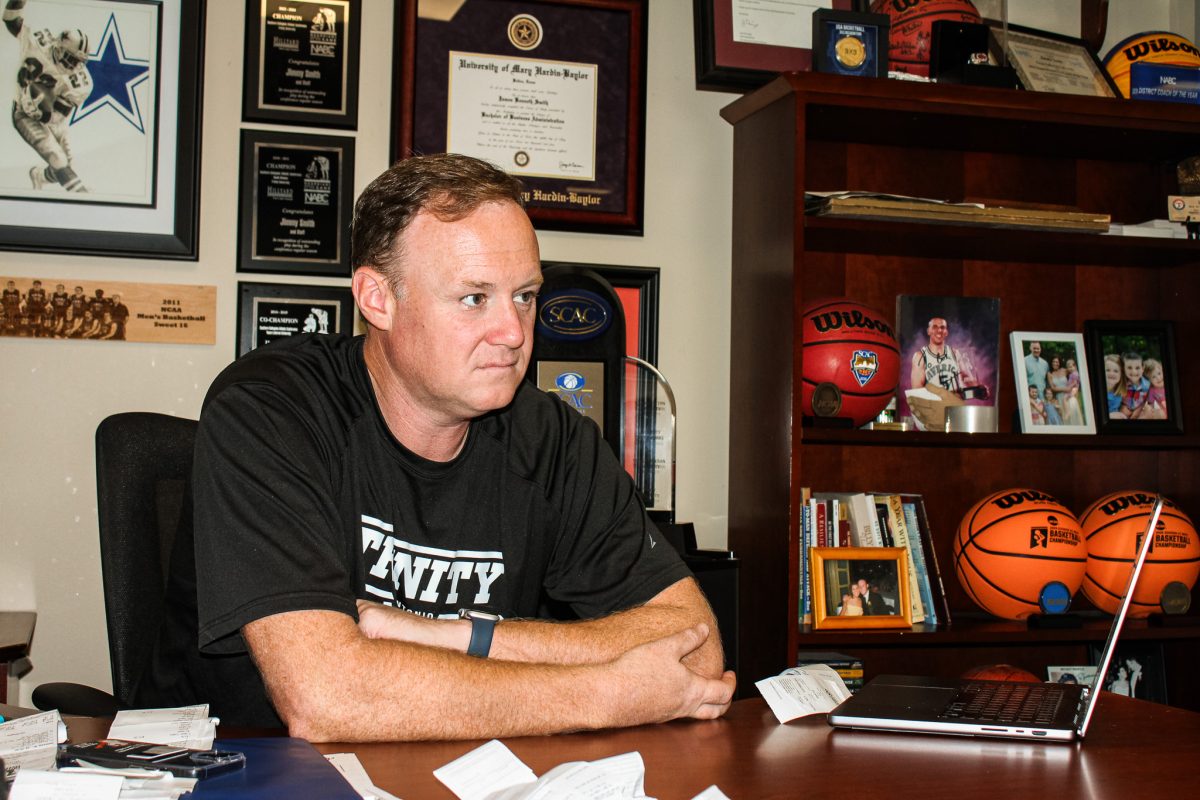 Coach Smith sits in his office surrounded by basketball memorabilia and trophies.