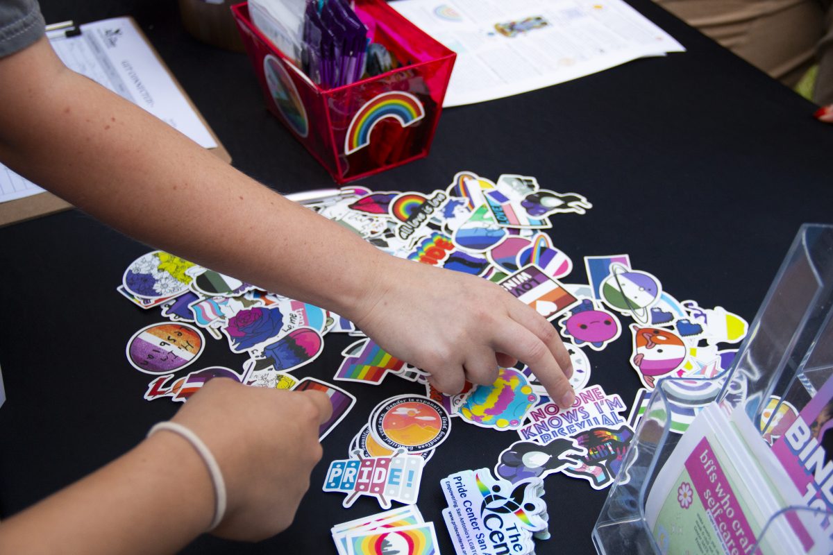 Students choose which stickers they want at the Pride Center San Antonio table at the Queer Health Fair